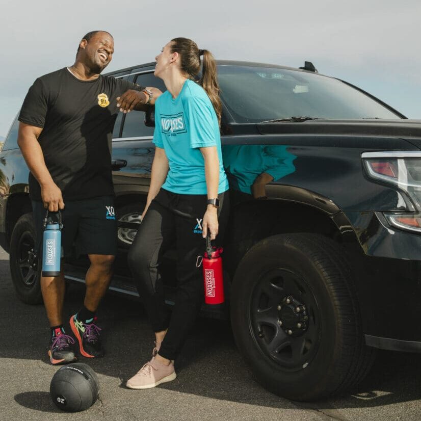 Two people laughing beside a parked car.